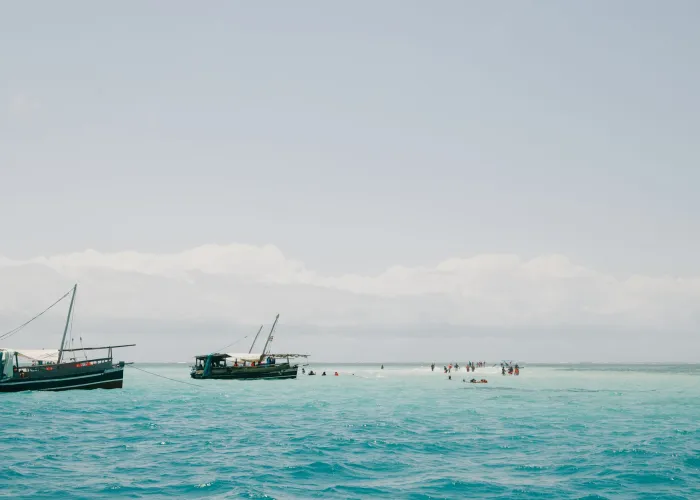 Traditional boats float in crystal-clear waters near Mombasa, Kenya, under a bright summer sky.