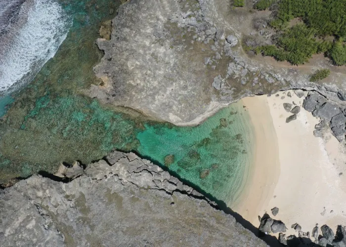 Stunning aerial shot of a secluded beach cove in Rodrigues, Mauritius, showcasing clear turquoise waters and rugged coastline.
