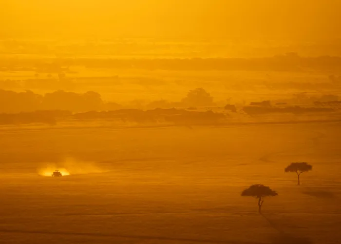 Dramatic view of Kenya's savanna during sunset. A vehicle drives through the golden landscape.