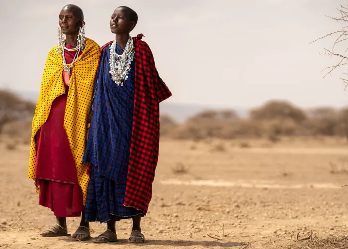 Masai individuals wearing vibrant traditional robes stand in the Tanzanian desert.
